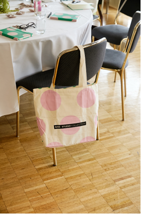 Tote bag with pink polka dots hanging on a chair.